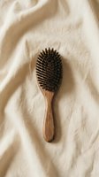 Natural wooden hair brush with boar bristles on soft beige linen fabric. Eco-friendly haircare tool for sustainable beauty routine and organic styling.
