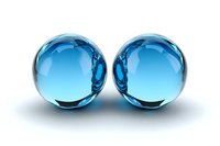 Two transparent blue glass or crystal spheres reflecting light on white background, symmetrical composition with mirror effect and soft shadows.