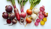 Fresh colorful beets and turnips collection with vibrant red, yellow and white varieties, some sliced showing beautiful ring patterns on white background.