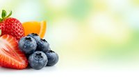 Fresh mixed berries strawberry blueberries orange slice on white background with green bokeh copy space for healthy eating organic food concepts.