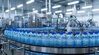 Rows of clear plastic water bottles moving along conveyor belt in modern beverage manufacturing facility with industrial equipment and machinery in background.