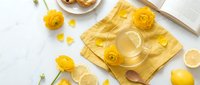 Bright yellow ranunculus flowers with lemon slices and honey on white marble surface. Fresh spring flatlay composition for wellness and natural beauty concepts.