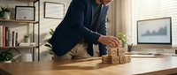 Man in business casual attire arranging wooden blocks with icons on desk, representing strategic planning, risk management, and corporate growth in modern office environment.