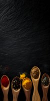 Colorful spices and seasonings in wooden spoons arranged on dark slate background with copy space, overhead view for food and cooking backgrounds.