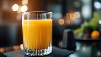 Fresh orange juice in crystal glass on dark table with blurred restaurant background and bokeh lights, morning breakfast drink concept.