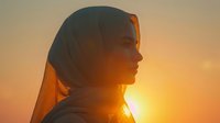 Young Middle Eastern woman in hijab silhouetted against vibrant orange sunset sky, side profile view capturing peaceful contemplative moment with sunlight creating ethereal glow.