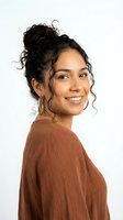 Happy young Hispanic woman with curly hair in messy bun wearing brown sweater smiling at camera on white background for lifestyle and portrait projects.