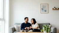 Modern couple relaxing on gray sofa in bright living room, enjoying coffee and conversation together in contemporary home interior design setting.