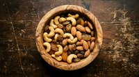 Mixed nuts and dried fruits in rustic wooden bowl on dark textured surface for healthy snacking and cooking ingredients.