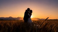 Romantic couple silhouette embracing in golden wheat field at sunset with mountain backdrop, love and togetherness concept for wedding photography.