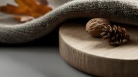 Minimalist autumn composition with pine cone and walnut on wooden board, soft textile and fallen maple leaf in warm natural lighting.