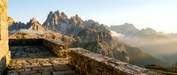 Scenic mountain landscape at sunrise with dramatic rocky peaks, golden light illuminating ancient stone ruins in foreground, misty valleys below, ideal for travel and nature projects.