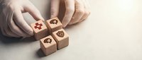 Hands arranging wooden blocks with healthcare medical icons including heart, cross and stethoscope symbols on neutral background for wellness concepts.