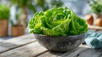 Fresh green lettuce leaves in stone bowl on wooden table for healthy cooking and salad preparation in modern kitchen setting.