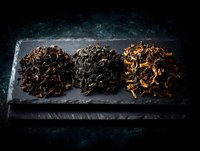 Three varieties of loose leaf tea arranged on dark slate board against textured black background, showcasing different fermentation levels and tea types.