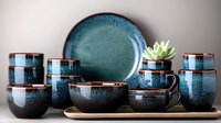 Ceramic tableware set in turquoise and black reactive glaze finish featuring cups, bowls, plates and decorative succulent pot arranged on wooden tray. Modern pottery collection.