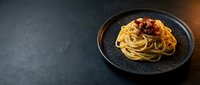 Spaghetti with crispy bacon and caramelized onions served on dark plate against slate background, ready for food photography, restaurant menus, cooking blogs.