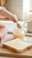 Young child with light skin tone spreading honey on toast at breakfast table with wooden dipper and jar for food preparation and cooking content.