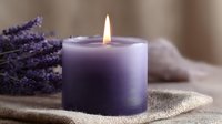 Glowing purple aromatherapy candle with fresh lavender sprigs on natural linen fabric creates peaceful spa atmosphere for relaxation and meditation practices.