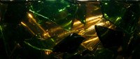 Shattered green glass fragments with golden light reflections creating dramatic shadows and highlights on dark surface for luxury design projects.