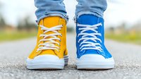 Mismatched yellow and blue canvas sneakers with white laces on asphalt road, wearing blue jeans, creative fashion concept showing individuality and unique style.
