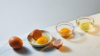 Fresh brown eggs with separated yolks in glass bowls on clean white surface for cooking and baking recipes.