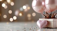 Elegant gift box with pink balloons and heart decorations on white surface with warm bokeh lights background for celebrations and special occasions.