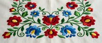 Traditional folk embroidery with colorful flowers and green vines on white fabric. Decorative floral pattern with red and blue blooms for textile design projects.