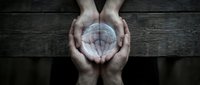 Hands cupping glowing crystal ball on dark wooden surface symbolizing fortune telling, mysticism, spirituality and magical predictions for divination concepts.