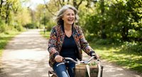 Happy mature woman riding vintage bicycle in sunny park path, enjoying active lifestyle and outdoor recreation in natural green environment.