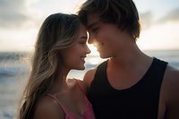 Young romantic couple sharing intimate moment at sunset beach, faces close together with soft natural backlight creating dreamy atmosphere. Tender summer love scene.
