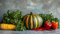 Fresh autumn harvest with striped green pumpkin, yellow corn, red bell peppers, chili peppers and parsley against dramatic stormy sky background on concrete surface.
