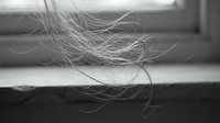 Close-up of delicate hair strands flowing in soft light with blurred background, capturing natural texture and movement in monochrome artistic style.