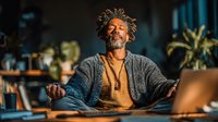 Peaceful African American man with dreadlocks meditating in lotus position at home, practicing mindfulness and yoga for mental wellness and relaxation.