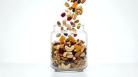 Mixed nuts and dried fruits falling into glass jar on white background, isolated for packaging design, recipe blogs, nutrition content, and healthy snack marketing.