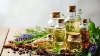 Essential oils in glass bottles with cork stoppers surrounded by fresh herbs, lavender, and spices on wooden surface for aromatherapy and natural wellness.
