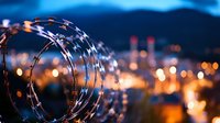 Razor wire coil silhouetted against blurred urban nightscape with glowing bokeh lights creating dramatic contrast between security and city ambiance.