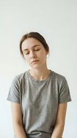 Young Caucasian woman with closed eyes in gray t-shirt practicing mindfulness meditation against neutral background for wellness and mental health concepts.