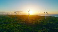 Wind turbines on green hills at golden sunset, aerial view of sustainable energy farm with spinning windmills generating renewable power against orange sky.