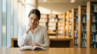 Young Asian woman reading book in modern library, studying at wooden table with natural lighting, academic research and education concept.