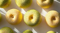 Fresh Asian pears arranged in rows casting dramatic shadows on white surface, showing detailed spotted skin texture and natural organic patterns.