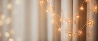 Warm golden heart-shaped string lights creating romantic ambiance against soft beige curtains with dreamy bokeh background for Valentine's Day decor.