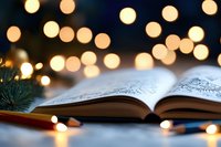 Open book with decorative pages against blurred warm bokeh lights and pine branch, creating magical cozy atmosphere for reading and relaxation.