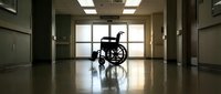 Empty wheelchair silhouette in hospital corridor with natural light from window creating dramatic shadows on polished floor for healthcare concepts.