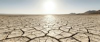 Cracked, parched earth stretches across an arid desert landscape under a hazy sun, depicting severe drought and climate change impacts for environmental awareness campaigns.