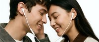 Young Asian couple sharing earphones, foreheads touching, smiling with eyes closed, enjoying music together in a romantic moment.