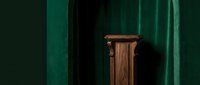 Elegant wooden pedestal stand against rich green velvet curtain backdrop, creating a luxurious display setting for product presentation.