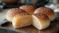 Fresh baked sesame seed hamburger buns with golden brown tops on wooden cutting board, soft fluffy texture perfect for burgers and sandwiches.