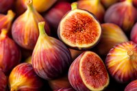Fresh ripe purple figs cut in half showing juicy red flesh and seeds, whole fruits arranged on dark background in natural lighting, macro food photography.