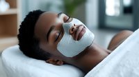 Young African American woman relaxing with white facial mask treatment at spa, lying on massage table during skincare procedure, wellness and beauty concept.